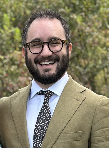 Ethan Kutlu smiles and wears a brown suit