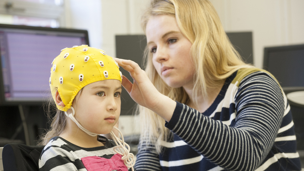 student placing electrode cap on young child research subject